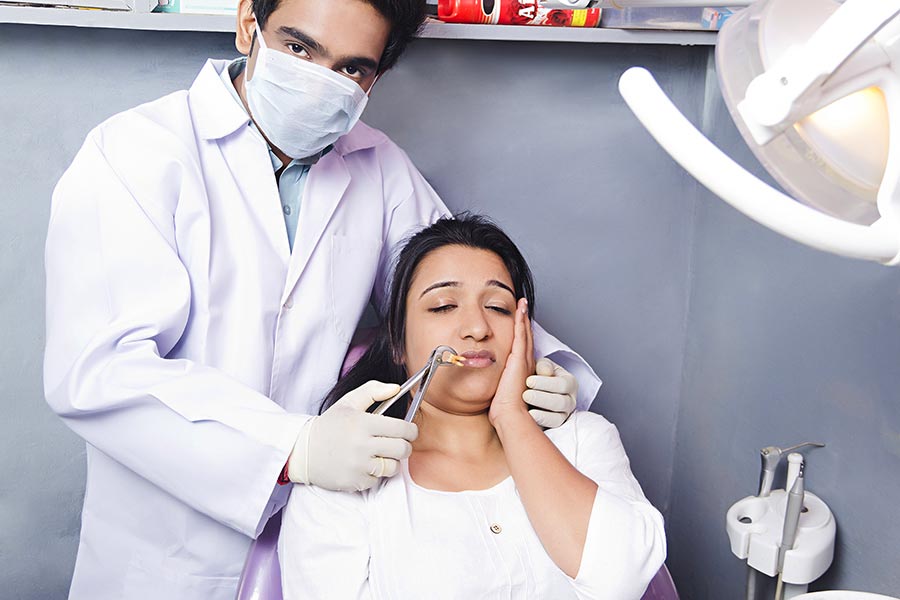 Indian Male dentist removes the tooth patient at the dental clinic