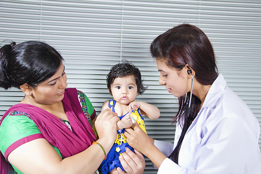 Doctor checking baby boy being carried by mother in-clinic Hospital