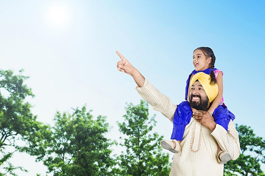 happy-punjabi-family-father-carrying-kid-daughter-on-shoulders-pointing