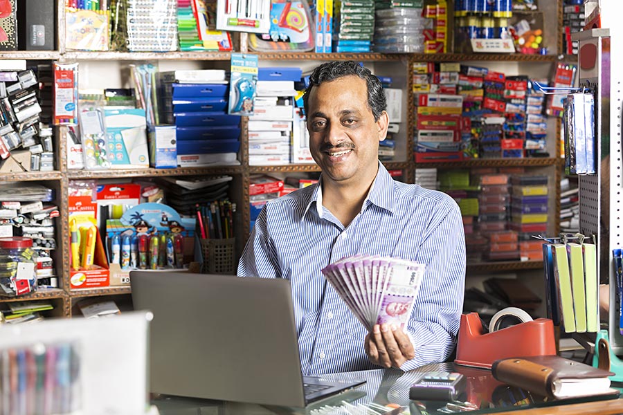 Indian Shopkeeper Man Using Laptop And Showing Money Stationary Shop