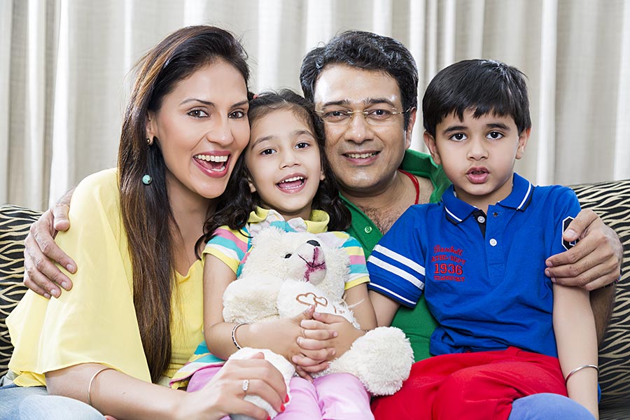 Indian Mothe And Father With Kids Sitting On Sofa At-Home